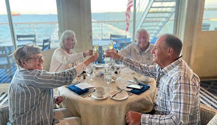 Two couples sit together at a round dinner table having a toast with their champagne glasses before a meal aboard a cruise.